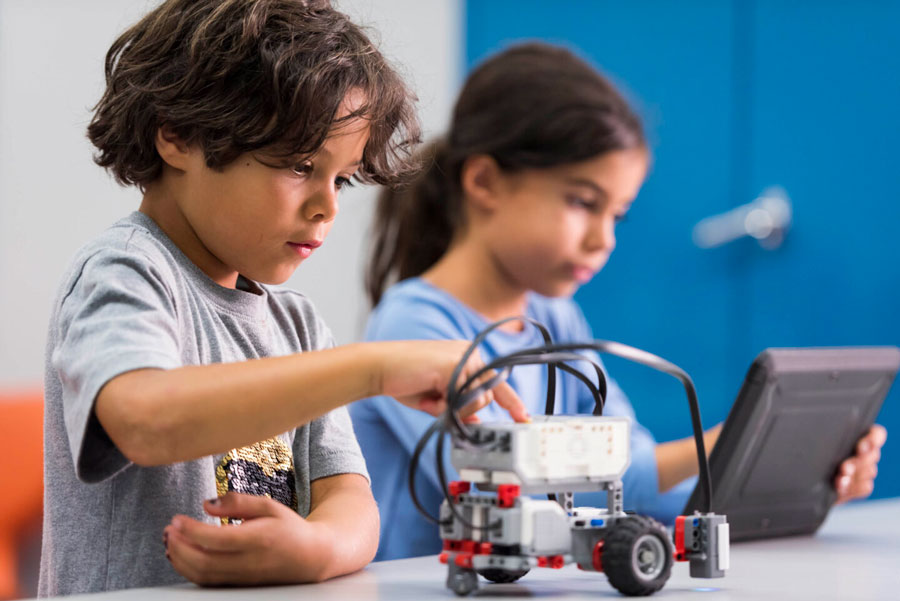 A child pushes a button on a robot and another child uses an app on a tablet for their robot construction