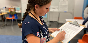 An educator writes on a clipboard.
